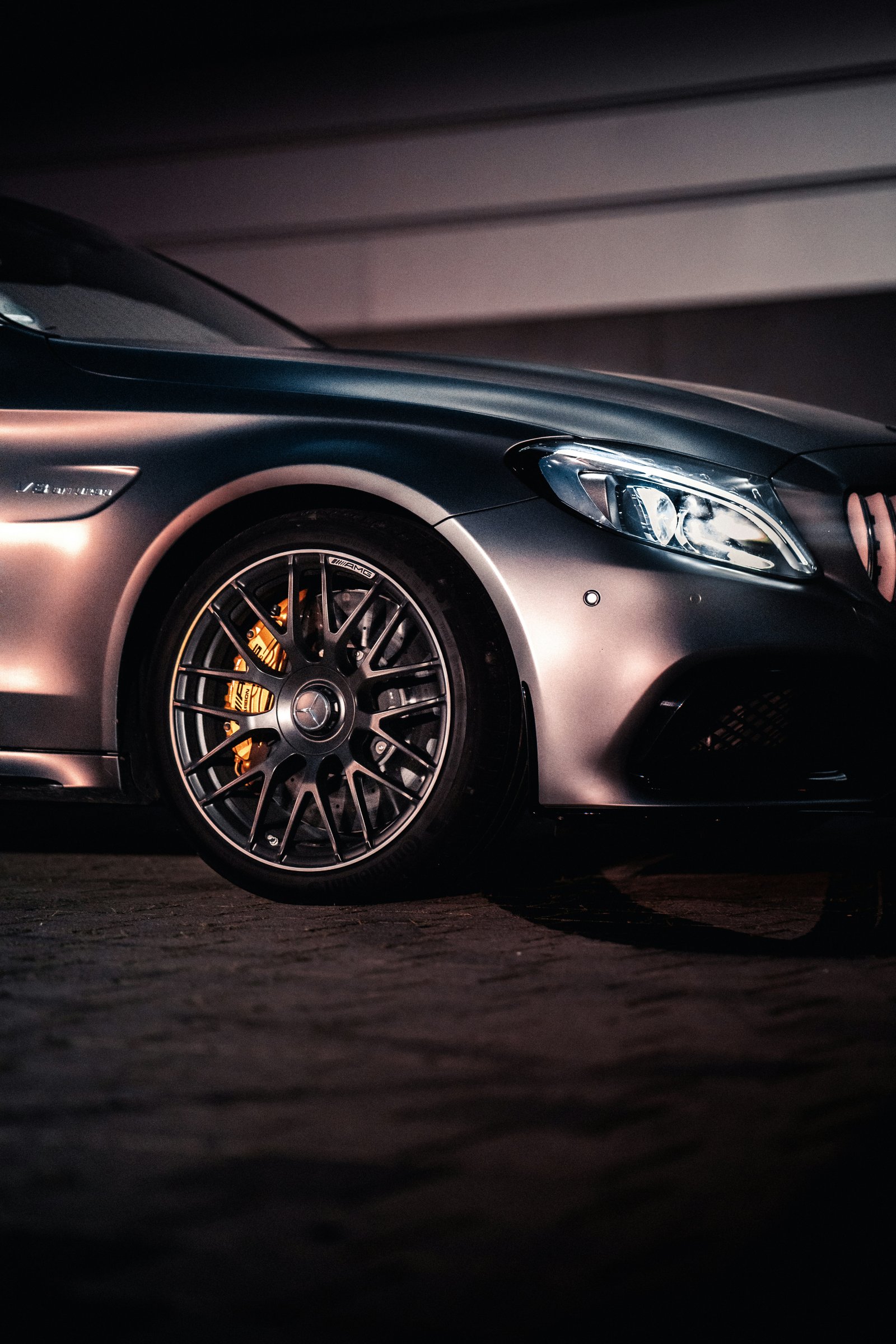 Mercedes-AMG C63 S forged wheel and glowing yellow brake caliper detail under workshop lighting.