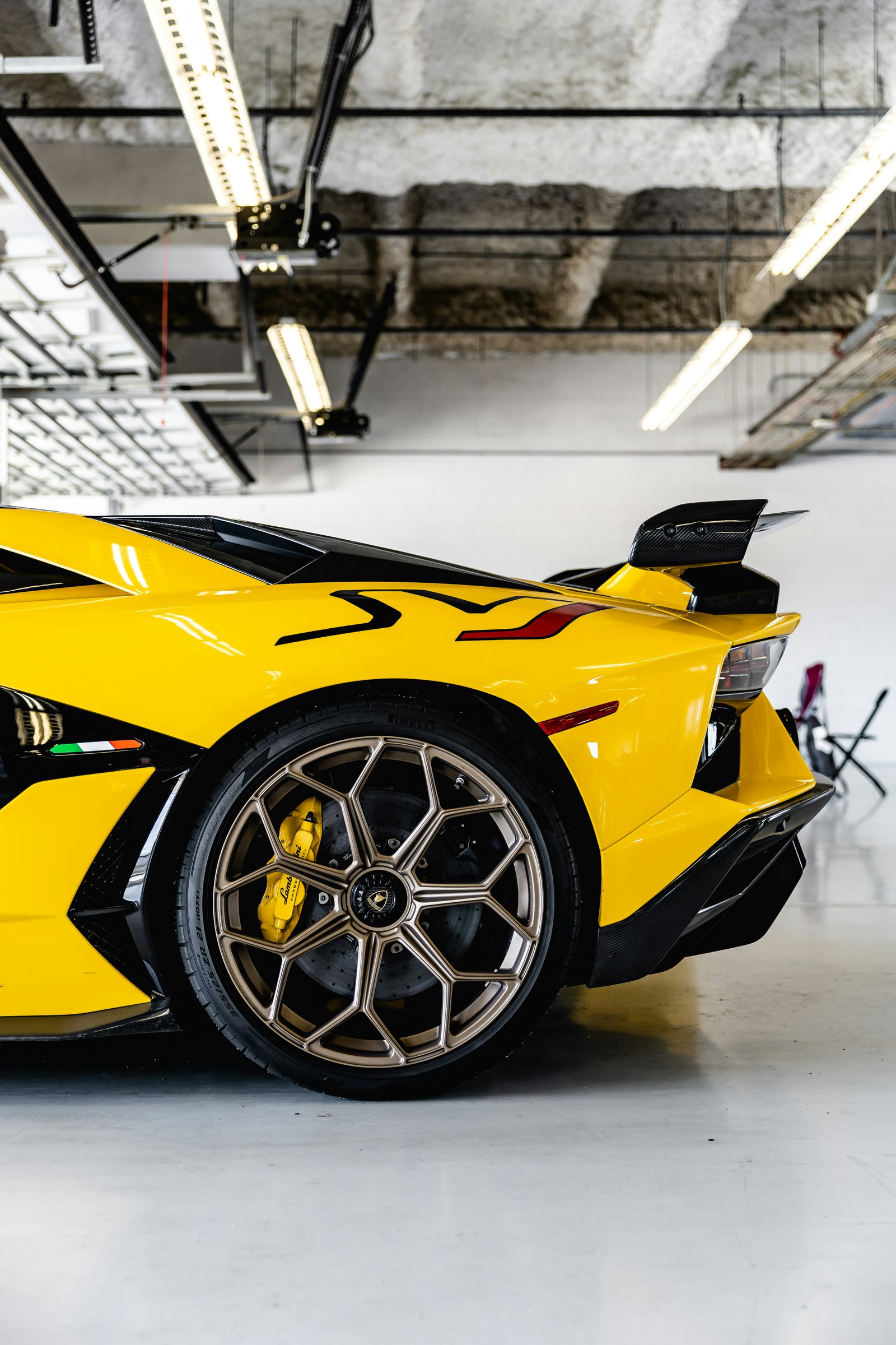 Lamborghini Aventador SVJ in Giallo Orion, rear quarter panel in a detailing studio showing the full aero wing and forged wheel.