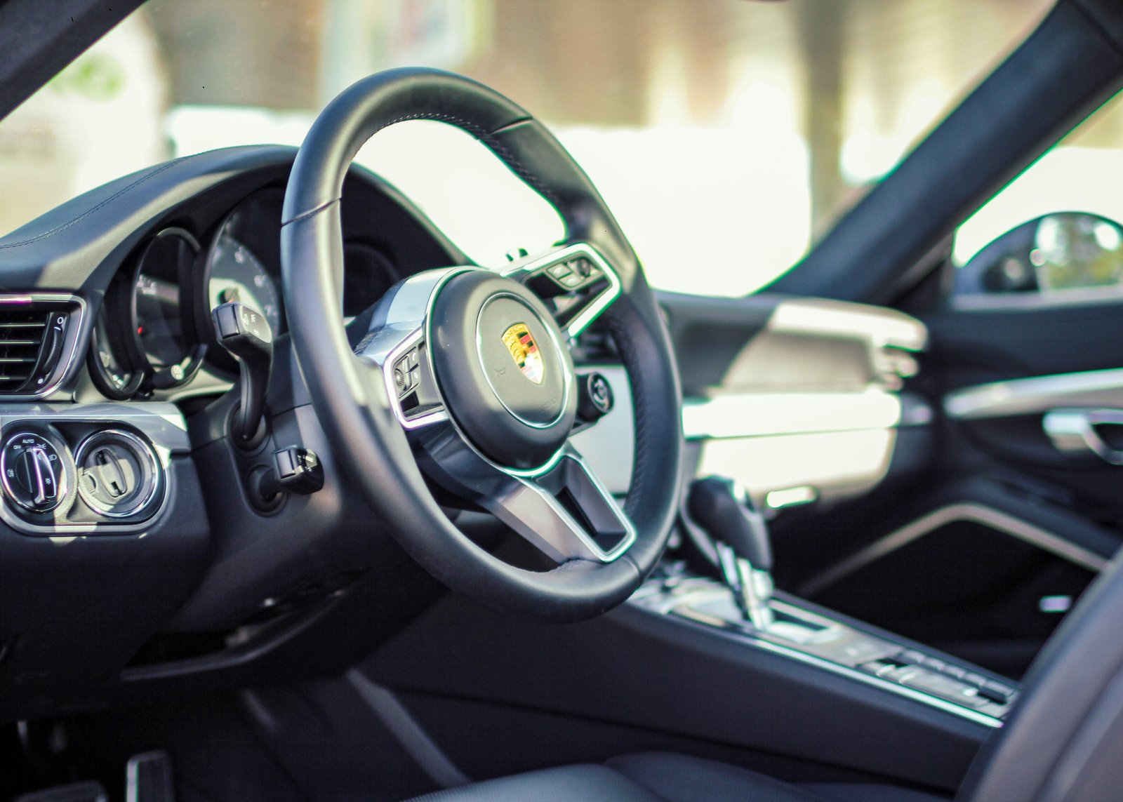 Porsche 911 Turbo S black leather cabin with sport steering wheel and yellow Porsche crest badge.